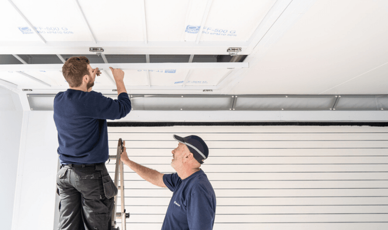 Two men installing an air filter inside a spray booth to keep it clean - Installing Air Filters