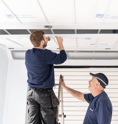 Two men installing an air filter inside a spray booth to keep it clean - Installing Air Filters